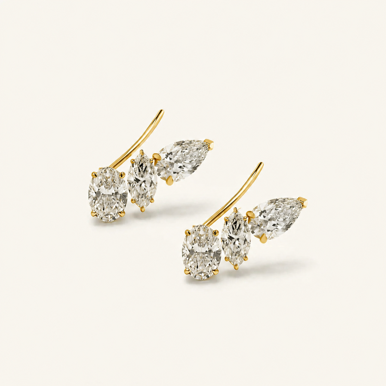 Gold illusion climber earrings with pear-shaped diamonds on a beige background